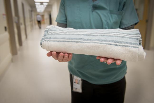 A Yukon Hospitals employee holds clean, white striped linens.