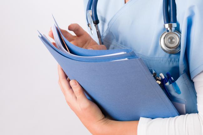 A nurse holds a folder of paper files. 